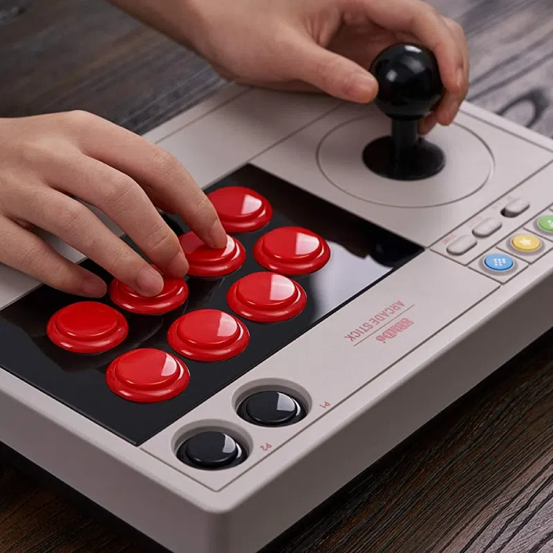 Arcade stick 8BitDo utilisé à deux mains avec joystick et boutons rouges